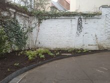 Een kleine stads tuin waar een deel van het terras verwijdert is en een verscheidenheid aan planten de ruimte inneemt.